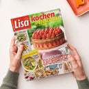 Magazintitel „Lisa kochen & backen“ in roten, gelben und weißen Schriftzügen auf grünem Hintergrund, gehalten von zwei Händen über hellem Tisch. Auf dem Cover eine Erdbeer-Schoko-Torte mit Schichten aus Sahne und Schokolade, sowie Textzeilen wie „Himmlisch backen mit Erdbeeren“, „Spargel-Küche“, „Praktisch & lecker“ und „Extra 16 Seiten Spar-Rezepte“, daneben mehrere Fotos von Gerichten wie Spargel, Gebäck und Salaten.