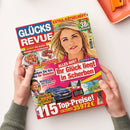 Titelblatt der Zeitschrift „Glücks Revue“ mit großem Porträt einer blonden Frau mit goldener Krone und schulterlangem Haar vor gelbem Hintergrund. Um das Hauptbild herum mehrere Schlagzeilen, darunter „Ihr Glück liegt in Scherben“, „Lecker! Die besten Rezepte zum Schlemmen“ und „Gewinnen Sie Ihr neues Auto“. Farbliche Gestaltung in Rot, Gelb und Blau, mit kleineren Fotos von Autos, Desserts und einer männlichen Person links unten.