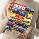 Person in beigefarbenem Pullover hält das Magazin „Auto“ mit rotem Schriftzug im oberen Bereich. Das Cover zeigt mehrere Autos verschiedener Marken wie VW, Toyota, Audi, Hyundai, Alfa Romeo und Renault in unterschiedlichen Farben vor neutralem Hintergrund. Zentrale gelbe Schlagzeile: „Der bessere Kauf!“, weitere Texte u. a. „Spannendes Mittelklasse-Duell“ und „Zwei mit Sechszylinder-Turbodampf“.