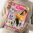 Helle, langärmlig gekleidete Person hält ein farbenfrohes Magazin mit pinkem Rand und dem Titel „Lissy“. Auf dem Cover groß abgebildet ein braunes Pferd in Bewegung, dazu kleinere Bilder weiterer Pferde, zwei reitende Personen mit Text „Fotoroman – Lola in Gefahr“, Unterzeile „Coole Punkte Appaloosa“, Aufdrucke wie „2 bezaubernde Poster!“, „Teste dein Lissy-Wissen!“ und „Spannende Comic“, umgeben von bunten, tierähnlichen Figuren.