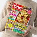 Magazin „tina Koch & Back-Ideen“ mit rotem Titelkopf und gelber Unterzeile „Genuss für jeden Tag“, gehalten von einer Person in beigefarbenem Strickpullover. Auf dem Cover ein Auflaufgericht mit Hähnchenteilen, Zitronenscheiben und Gemüse; sichtbare Texte: „Schlemmer-Hits mit Huhn“, „Saftig-süße Erdbeerkuchen“, „Große Pasta-Liebe“, „Gratis-Extra“ und „Mehr als 100 Rezepte mit Geling-Garantie“.
