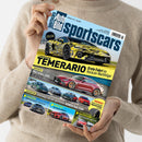 Hellhäutige, geschlechtsneutrale Person in beiger Strickkleidung hält das Magazin „Auto Bild sportscars“ (Ausgabe Juni 2025) mit hellblauem Titel und mehreren Autos darauf. Hauptmotiv ist ein gelb getarnter Lamborghini mit der Überschrift „Lamborghini Temerario – Erste Fahrt im Huracán-Nachfolger“. Weitere sichtbare Texte: „Mercedes-AMG GT 63 Pro 4Matic+“, „Vergleich“, „Einzeltest“, „Kaufberatung“, „Reifentest“, „Handschartern“.