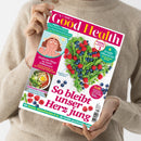 Hellbeigefarbener Pullover, neutrale Person hält das Magazin „Good Health“ Ausgabe Mai/Juni 2023 mit farbigem Titelblatt. Haupttitel „So bleibt unser Herz jung“ über einem Herz aus grünen Bohnen, Erbsen, Himbeeren und Blaubeeren. Weitere Texte: „Einfache Wege zu mehr Selbstwert“, „Sattmacher-Frühstück“, „Das Einmaleins des Sonnenschutzes“ und „Straffe Oberarme“. Farbtöne: Rot, Grün, Blau, Weiß und Gelb.