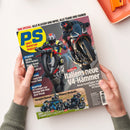 Titelblatt des „PS sport motorrad magazin“ mit zwei Motorradfahrer*innen in Rennkleidung auf zwei schwarzen Sportmotorrädern in dynamischer Fahrposition. Schlagzeilen u. a.: „Italiens neue V4-Hämmer“, „Vergleichstest Power-Nakeds“, „Premiere Aprilia RSV4 Factory“. Oben gelbes Logo mit blauer Schrift, Hintergrund grau-blau und rötlich, gehaltene Hände im unteren Bildbereich.