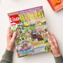 Zwei Hände halten die Juni-2025-Ausgabe der Zeitschrift „Lisa Wohnen & Dekorieren“ mit rosa und gelbem Titeltext „Lasst uns einfach feiern!“. Auf dem Cover sind ein sommerlich dekorierter Terrassenbereich mit Sofa, bunten Kissen und gedecktem Tisch sowie ein kleines Zusatzheft „Rosen-Liebe“ mit Blumenarrangement abgebildet; weitere sichtbare Textelemente nennen Themen wie Dekoideen und Sommerfeste.
