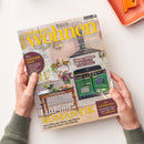 Titelblatt der Wohnzeitschrift „zuhause wohnen“, Ausgabe Mai 2026. Abgebildet ist eine wohnlich eingerichtete Küche mit hellrosa Wand, großem grünen Gasherd, Blumenstrauß auf Holztisch und Obstschale. Aufschriften u. a.: „Lust auf Romantik“, „Die schönsten Sideboards“, „Perfekt gepflegt – Effektive Tipps für makellose Oberflächen“, „Plus: Sommerfest“ und Gewinnhinweis über 5.000 Euro. Hände halten die Zeitschrift über hellem Hintergrund.
