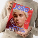 Frau in beigem Strickpullover hält das Magazin „jolie“ mit rotem Cover und großem lilafarbenem Schriftzug. Auf dem Titel ist eine Person mit kurzem, blondem Haar und neutralem Gesichtsausdruck zu sehen. Schlagzeilen: „Die neuen Trend-Labels“, „Stehen mir kurze Haare? Der Short-Check verrät’s“, „Streetstyles aus der ganzen Welt“ und „Die beste Investition deines Lebens“. Ausgabe Herbst 2023.