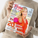 Person in beigefarbenem Strickpullover hält ein Magazin mit dem Titel „Frau im Leben“. Auf dem Cover eine lächelnde blonde Frau in rotem Kleid vor hellem Hintergrund. Sichtbare Schlagzeilen: „Das Glück festhalten“, „Wenn’s im Ohr pfeift und piepst“, „20 intime Fragen an die Frauenärztin“, „15 Sommer-Kleider“, „Schmuck mit Perlen“, „SÜSSE FRÜCHTE“. In der unteren Leiste Themen zu Wechseljahren und Kräutern.
