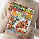 Person in beigem Strickpullover hält die Zeitschrift „meine gute Landküche“ mit sommerlichem Covermotiv, betitelt „So schmeckt der Sommer!“. Abgebildet sind Grillspieße mit Gemüse und Fleisch, eine Schale Dip, Pommes und Zitronenspalten. Weitere Texte: „Sonniger Genuss: Aprikosen-Kuchen“, „Liebling der Saison: Paprika neu entdeckt“, „Obst und Gemüse – jetzt kochen wir ein“, „Hausgemacht schmeckt’s am besten!“.