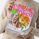 Helle, beidseitig gefaltete Food-Zeitschrift mit dem Titel „essen & trinken“ in pinker Schrift, gehalten von einer Person in beigefarbenem Strickpullover; auf dem Cover ein Teller mit gebratenem Fleisch, grünen Spargelstangen, Pommes frites und heller Sauce. Weitere sichtbare Texte: „Süße Sachen – von Cupcake bis Schokotorte“, „Schnell und gut – Frühlingsfrische Alltagsküche“ sowie Hauptüberschrift „Spargel, wie wir ihn lieben“.