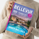 Person in beigem Strickpullover hält das Immobilienmagazin „BELLEVUE“ mit blau-violettem Titelblatt. Das Cover zeigt ein mediterranes Anwesen mit Pool bei Abendlicht, heller Steinbau, Wasserreflexionen und Palmen. Sichtbare Texte: „BELLEVUE – Europas größtes Immobilien-Magazin“, „Immer Mallorca“, „Frankfurt – über 30 Extraseiten“, „800 Angebote aus aller Welt“, „Österreich“, „Italien“, „Investment“ und „Lübeck & Co“.