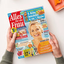 Titelblatt der Zeitschrift „Alles für die Frau“, gehalten von zwei Händen über hellem Hintergrund. Im Mittelpunkt steht eine lächelnde blonde Frau vor blauem Hintergrund. Auf dem Cover sind Texte u. a.: „5 Kilo leichter in nur 1 Woche“, „Jetzt richtig vorsorgen“, „Raffinierte Rührkuchen“, „Farbenfrohe Mode-Stars für den Sommer“ und „24 Pfund weg“. Mehrere bunte Textfelder mit Rezept-, Gesundheits- und Modethemen umrahmen das Porträt.