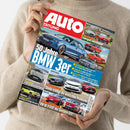 Person in beigem Strickpullover hält die Zeitschrift „Auto Zeitung“ in den Händen, deren Titelblatt einen blauen BMW und weitere Autos in verschiedenen Perspektiven zeigt. Sichtbare Überschriften: „50 Jahre BMW 3er“, „Skoda schlägt die deutschen Premiums!“, „VW ID.3 GTX: der bessere GTI?“ sowie kleinere Texte zu Marken wie Mini, Aston Martin und Jeep, vor rotem und blauem Hintergrund mit weißer Schrift.