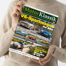 Person in beigem Strickpullover hält die Zeitschrift „MotorKlassik“ mit grün-gelbem Titel und mehreren Farbfotos klassischer Autos. Hauptüberschrift „V6-Sportwagen der 80er“, darunter Fahrzeuge wie Alfa Romeo GTV6, Ford Capri 2.8i, Renault Alpine A310 V6, Porsche 911 Carrera 3.2, Maserati A6GCS Spyder und Renault Sport Spider, dazu Textfeld „Traum-Tour USA im Mercedes W123“ vor landschaftlichem Hintergrund.