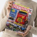 Person in beigem Strickpullover hält Magazin „Fernfahrer – Das Truck-Magazin“. Auf dem farbintensiven Cover ist ein roter Lkw mit gelbem Frontgrill und gelber Aufschrift „wolter-koops-logistik.de“ zentral abgebildet. Umgebende Textfelder zeigen Themen wie „Wohlfühl Trucks“, „Alte Fuhrparks, neue Lösungen“ und kleinere Bilder von weiteren Lkw-Modellen in Gelb, Blau und Grün vor grauem Hintergrund.