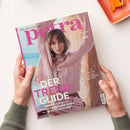 Titelbild der Zeitschrift „petra“ mit einer weiblichen Person in einem hellrosafarbenen Zopfpullover und roséfarbener Tasche vor beigefarbenem Hintergrund. Aufschriften: „Mein Leben! Mein Luxus!“, „DER TREND-GUIDE“, „Traumkleider +++ IT-Bags +++ Summer Shoes +++ Beauty-Highlights“, „STIL & HALTUNG“, „BEST OF GERMANY“. Gehalten von zwei Händen mit grünem Strickpullover vor hellem Hintergrund mit orangefarbener Schale.