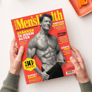 Titelbild der Zeitschrift „Men’s Health“ mit rotem Hintergrund, gelbem Schriftzug und einem schwarz‑weiß Foto eines muskulösen älteren Mannes, der oberkörperfrei posiert und mit einer Hand seine Hose leicht herunterzieht. Mehrere Schlagzeilen in Gelb und Weiß, darunter „Stärker in jedem Alter“, „Endlich schlank“, „Härte Test“ und ein gelbes Sechseck mit der Aufschrift „30 Jahre Men’s Health“. Hände halten das Magazin über hell beigem Untergrund.