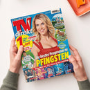 Titelseite der Zeitschrift „TV direkt“, Ausgabe Nr. 12 vom 31. Mai bis 13. Juni 2025. Im Mittelpunkt steht eine lächelnde hellblonde Frau in rotem Kleid vor blauem Hintergrund. Überschriften u. a.: „Ihr bestes Programm zu PFINGSTEN“, „14 Tage volles Programm“, „Fußball Nations League“, „Jetzt mit Mediatheken-Planer“. Weitere Bilder zeigen TV-Szenen, Naturmotive und Prominente. Zwei Hände halten das Magazin über einem weißen Tisch mit orangefarbener Schale.
