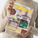 Beige gekleidete Person hält die Wohnzeitschrift „zuhause wohnen“ in beiden Händen, Titel in Gelb und Weiß, Ausgabe Mai 2026. Auf dem Cover: eine helle Küche mit grüner Herdkombination, Holztisch, Vase mit violetten Blumen und Fensterausblick. Sichtbare Textinhalte: „Lust auf Romantik“, „Plus: Sommerfest“, „Panorama-Reisen“, „Die schönsten Sideboards“, „Perfekt gepflegt“, „Zu gewinnen“.