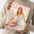 Person in heller Strickjacke hält eine Zeitschrift mit dem Titel „Verena Stricktrends“. Auf dem Cover ist eine weibliche Person in einem weißen gehäkelten Kleid am Strand zu sehen. In pinker und schwarzer Schrift stehen Textzeilen wie „54 exklusive Designs“, „Heiss in Weiss“, „Dark Shades“, „Let’s go to the Beach“ und „Maschenleicht durch den Sommer“. Hintergrund in Sandfarben, Perspektive leicht von oben.
