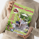 Eine Person in beigefarbenem Pullover hält ein Magazin mit hellgrünem Titelblatt „Wohnen & Garten – Juni 2025“. Auf dem Cover ist ein sommerlich dekorierter Garten mit Esstisch, Stühlen, Blumen und Sonnenschirm zu sehen. Textinhalte u. a.: „Willkommen im Sommersalon“, „Wohnen“, „Garten“, „Dekorieren“, „Garten & Blumen“ sowie Hinweise zu Ideen, Kräutern, Rosenpflege und Rezeptvorschlägen mit Kirschen.