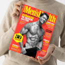 Titelbild der Zeitschrift „Men’s Health“ mit einem muskulösen, männlichen Oberkörper in Schwarz-Weiß vor rotem Hintergrund, gelbem und weißem Text. Überschriften: „Stärker in jedem Alter“, „Endlich schlank“, „Härte-Test“, „Super? Mann!“, „30 Jahre Men’s Health“ in gelbem Sechseck. Eine Person in beiger Strickjacke hält das Magazin mit beiden Händen vor neutralem Hintergrund.