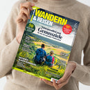 Person in beigefarbenem Strickpullover hält das Magazin „Wandern & Reisen“ (Ausgabe 03-26 Sommer) mit Titeltext „Naturparadiese und Genussziele für eine unvergessliche Wandersaison“. Coverbild zeigt zwei wandernde Personen mit Rucksäcken und Hut auf grünem Hügel mit Blick auf Landschaft, weitere sichtbare Texte: „Ratgeber: Blasen verhindern“, „Premium-Wanderwelten“, „50 frische Ideen“, „Süddeutschland Deluxe“, „Traumhafte Alpenziele“, „Osterspaier Langhalsweg“.