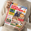 Person in beigem Strickpullover hält das Magazin „selber machen! DIY – Bauen | Gestalten | Renovieren“ hoch, Titelbild mit einem Mann beim Bau einer Holzterrasse. Textausschnitte: „TERRASSEN-IDEEN selber realisieren“, „RATGEBER LASUREN UND LACKE“, „Innovative MÄHROBOTER“, „KUSCHELPLÄTZE“, „Kochen unter freiem Himmel“. Cover zeigt Holzterrassen, Werkzeuge und Bauanleitungen in roter, gelber und weißer Schriftgestaltung.