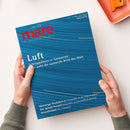 Zwei Hände mit grünen Strickärmeln halten eine Ausgabe der Zeitschrift „mare – Die Zeitschrift der Meere“, No. 176, mit blauem, wellenförmig strukturiertem Cover und rotem Logo. Haupttitel „Luft“ mit Unterzeilen „Schnupperkurs in Tasmanien. Hier weht die sauberste Brise der Welt“ sowie weiteren Themen: „Meerenge Dschibuti“, „Die Splash-Formel“ und „Strandfußball Rio in Rostock“, auf hellem Tisch neben orangefarbenem Tablett.