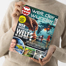 Person in beigem Strickpullover hält das Magazin „welt der wunder“ in beiden Händen, Titel mit großem weißen Schriftzug und rotem Logo oben links. Hauptüberschrift: „Wer beherrscht die Welt? Im Jahr 2030“, darunter Themen zu Militär, Energie, KI; auf dem Cover eine Hand, die Schachfiguren auf einem Brett bewegt, im Hintergrund Weltkarte mit Leuchtpunkten sowie kleinere Teaser zu Gesundheit, Natur und Geschichte.