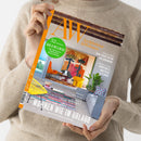 Person in beigem Strickpullover hält die Zeitschrift „AW Architektur & Wohnen“ mit orange-weißer Titelleiste und großem Innenraumbild mit bunter moderner Einrichtung. Sichtbare Texte: „52 Seiten Bad & Wellness – die 100 besten Badstudios Deutschlands“, „Wohnen wie im Urlaub – Häuser an Sehnsuchtsorten“, „Neue Architektur aus Dänemark“, „Kunstvolle Muster & Texturen“.