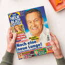Titelbild der Zeitschrift „Das Neue Blatt – Das Original!“ mit einem lächelnden Mann im weißen Hemd vor blauem Hintergrund. Mehrere Schlagzeilen in Gelb, Rot und Blau, darunter „ROLAND KAISER – Noch eine neue Lunge!“, „Die große Hoffnung“ und Themenfelder am unteren Rand wie „KÖNIGIN MAXIMA“ und „MATTHIAS REIM“. Ein kleineres Porträt einer Frau links oben, gehalten von zwei Händen über hellem Tischuntergrund.
