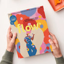 Titelmagazin „flow“ mit gelbem Schriftzug vor abstraktem, bunt gepunktetem Hintergrund in Rot-, Rosa-, Blau- und Gelbtönen; im unteren Bereich eine zeichnerische Darstellung einer weiblichen Person in blauer Latzhose mit farbigen Blumenmustern und kurzärmeligem Oberteil, die einen Pinsel hält. Oberer Randtext: „Das Magazin für persönliche Entwicklung, Kreativität & mehr Ruhe“. In zwei Händen über hellem Untergrund gehalten.