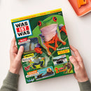 Magazincover der Kinderzeitschrift „WAS IST WAS“ Nr. 5 mit grünem Hintergrund; zentral abgebildet ist ein farbenfroher Frosch mit roten Augen und orangefarbenen Beinen. Sichtbare Texte: „Themen: Schwimmende Autos, Frösche, Kaulquappen“, „Amphibien – Leben im Wasser und an Land“, „Wetter – Zerstörerische Winde“, „Märchen – Menschen, die zu Tieren werden“, „Seeotter – Schlau und dickes Fell“, „2 tolle Poster“. Gehalten von zwei Händen über hellem Tisch.