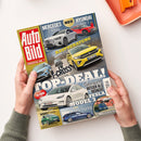 Titelblatt der Zeitschrift „Auto Bild“ mit rotem Logo auf gelbem Hintergrund, Untertitel „Europas Nr. 1“. Abgebildet sind mehrere Autos, darunter ein silberner Mercedes C-Klasse mit dem Schriftzug „NEU“, ein roter Hyundai Ioniq 3, ein gelber VW T-Cross mit „Kaufberatung“, unten ein weißer Tesla Model 3 mit Text „Top-Deal! Gebraucht besser als gedacht“, daneben kleinere Bilder eines grünen Renault Twingo und eines blauen BMW M340i Touring. Hände halten das Magazin auf hell beigem Untergrund.