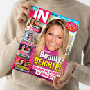 Person in beigefarbenem Strickpullover hält das Magazin „IN“ in beiden Händen, Titel in pink-weißem Schriftzug. Auf dem Cover eine lächelnde Frau mit blondem Haar in pinkem Oberteil, Überschrift „Beauty-Beichte! So steht sie wirklich zu Botox & Co.“; linke Spalte mit kleineren Porträtfotos und Texten wie „Noch ein Baby?“, „Psycho-Klinik“, „Schlimme Vorwürfe“, „Todes-Nacht?“ sowie weiteren Schlagzeilen zu Promi-Themen.