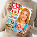 Person in beigefarbenem Strickpullover hält eine Ausgabe der TV-Zeitschrift „BILD + FUNK“ in den Händen. Auf dem Cover ist eine blonde Frau mit blauem Oberteil vor hellem Hintergrund abgebildet, daneben Texte wie „Herzhafte Grill-Rezepte“, „Sommerliche Köstlichkeiten mit Fisch, Fleisch oder Gemüse“, „Wie wird unser Wetter?“ und „Ein TV-Liebling wird 70“. Farbliche Gestaltung in Rot, Weiß, Gelb und Blau.