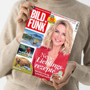 Person in beigem Strickpullover hält Zeitschrift „BILD + FUNK“ mit rotem Titelbereich und Porträt einer lächelnden blonden Frau im roten Oberteil. Sichtbare Schlagzeilen: „Neue Lieblingsrezepte – Herrlich würzig & leicht gemacht“, „Urlaub am Wasser – Die schönsten Seen in Deutschland & Österreich“, „Eine junge Mutter wird entführt“ und „Was kleine Bären lernen müssen“.