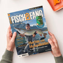 Titelcover des Magazins „Fisch & Fang – Das Erlebnis-Magazin für Angler“, gehalten von zwei Händen über einer hellen Tischfläche. Auf dem Cover ist ein männlicher Angler in grauer Kleidung und roter Kappe zu sehen, der einen großen Hecht vor einer See- und Bergkulisse hält. Textelemente: „Hechte mit Hybridköder“, „Heiße Platte“, „Auf Achse“, „Schnelle Tonne“ sowie Hinweis auf ein Extra-Teil „Bissfarbenguide“.