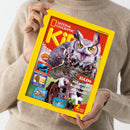 Person in beigefarbenem Pullover hält eine Ausgabe des Magazins „National Geographic Kids“ mit gelbem Rand. Auf dem Titelbild ist eine Eule mit weit geöffneten gelben Augen und ausgebreiteten Flügeln zu sehen, darüber der Text „EULEN: Mit großen Augen durch die Nacht!“. Links befinden sich kleine Bilder mit Texten zu „ORCAS“, „PHARAONEN“ und „DINOSAURIER“, unten der Hinweis „2 starke Poster!“.