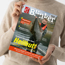 Schräg gehaltene Angelzeitschrift „Blinker“ mit rotem Fischlogo und dem Zusatz „Europas größte Angelzeitschrift“. Auf dem Cover hält ein männlicher Angler einen großen Fisch; sichtbare Texte: „Fliegenfischen“, „Hotspots im Fluss“, „Norwegens spannendster Räuber Heilbutt“, „Spinnfischen light“, „Naturköder light“ und „Wieso mm-Angaben bei Geflecht reine Fiktion sind“. Beige gekleidete Person hält das Magazin mit beiden Händen.