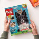Titelbild der Tierzeitschrift „Ein Herz für Tiere“ mit großem Porträt eines schwarz-weißen Hundes, hinter dem eine graugetigerte Katze hervorschaut, auf blauem Hintergrund. Überschrift: „Wie heißt du denn? Was Tiernamen verraten“. Oben rote Titelbox mit Herz-Logo und Text „Weil wir Tiere lieben“. Kleine Bilder links zeigen einen Hund mit Koffer, eine Katze am Fenster und eine Meeresschildkröte unter Wasser.