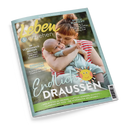 Titelbild des Elternmagazins „Leben & erziehen“ mit einer weiblich gelesenen Person in rot-weiß gestreiftem Oberteil, die ein Baby im blauen Strampler im Arm hält. Hintergrund zeigt grüne Natur. Textaufschriften: „Im Schlummer-Modus“, „Ordnung schaffen“, „Sprich Klartext!“ sowie großer Titel „Endlich Draußen“ mit gelber Sonne. Unterzeile: „Geburtstag im Grünen“, „Luftige Sommer-Outfits“, „Glamping mit Kids“, „Die schönsten Wildparks“.