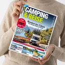 Weibliche Person im beigefarbenen Strickpullover hält eine diagonal ausgerichtete Zeitschrift mit dunkelblauem, weißem und neongelbem Cover; Titel „CAMPING & REISE“, Zusatz „EINFACH FREI SEIN.“ und „MAGAZIN“. Sichtbar sind ein Wohnmobil vor Berg- und Seelandschaft sowie die Texte „Routen ins Glück“, „Caravan Salon“, „Neuheiten 2027“, „Münsterland“, „Vogtland“, „Finnland“, „Südtirol“ und „Auvergne“.