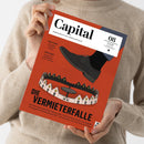 Person mit hellbeigem Strickpullover hält ein schräg fotografiertes, rotes Magazin mit weißem Titelbereich. Sichtbare Texte: „Capital“, „WIRTSCHAFT IST GESELLSCHAFT“, „CHINA-GEFAHR“, „AKTIVE FONDS“ und „DIE VERMIETERFALLE“; die Illustration zeigt einen schwarzen Schuh über einer Häuserreihe.