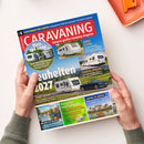 Auf weißem Tisch liegt schräg ein blau-rotes Magazin, das von zwei Händen gehalten wird. Titel „CARAVANING“, Untertitel „Europas großes Camping-Magazin“ sowie Texte zu „Schutzbriefe für Camper“, „Adria Alpina“, „Fendt Apero“, „Ratgeber und Zubehör“ und „Camping im Loiretal“; abgebildet sind Wohnwagen, ein schwarzes Auto, Landschaften und Campinganlagen.