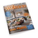 Titelbild der Wohnzeitschrift „zuhause wohnen“, Ausgabe Juli 2026, mit dem Schriftzug „Wie Wohnen wirklich glücklich macht“. Abgebildet ist ein modernes Wohnzimmer mit grauer Eckcouch, zahlreichen beigefarbenen und weißen Kissen, einem massiven Holztisch mit Dekoobjekten und Blumen, großem Wandspiegel und heller Tageslichtstimmung. Schlagzeilen u. a.: „Kleine Räume, viel Platz“, „Zaubern mit Tapeten“ und „Lust auf Süden“.