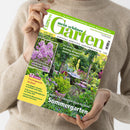 Helle, langärmlig gekleidete Person hält das Juni 2025‑Heft der Zeitschrift „mein schöner Garten“ vor neutralem Hintergrund. Das Cover zeigt einen farbenreichen Sommergarten mit grünen Pflanzen, blühenden Stauden und einem Holztisch mit Stühlen. Textelemente: „Unsere 50 schönsten Ideen für Ihren Sommergarten“, „Richtig düngen leicht gemacht“, „Duftende Stauden entdecken“, „12 Seiten Gartenpraxis im Juni“.
