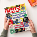 Aufgeschlagene CHIP-Zeitschrift mit rotem und weißem Titel, gehalten von zwei Händen mit grauen Strickbündchen; eine weibliche oder männliche Person ist nicht erkennbar. Sichtbare Überschriften sind „Tempo-Tricks für Windows 11“, „ARM-Chips: Power pur!“, „Festung FritzBox!“, „WLAN Security-Box“ und „Alle Videos gratis herunterladen“; daneben sind Softwareverpackungen, eine Laptop-Abbildung und ein orangefarbenes Tablett zu sehen.