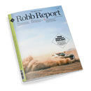 Magazin „Robb Report“ (deutsche Ausgabe, Nr. 38) mit hellblauem Titelhintergrund und grünem linken Seitenstreifen; unten Bild eines weißen Sportwagens, der auf staubiger Piste fährt und Staubwolken aufwirbelt. Aufdrucke u. a.: Titel „Robb Report“, Unterzeile „The New Luxury“, Textfeld mit Überschrift „Wer bremst, verliert“. Perspektive leicht schräg von oben, Magazin vor neutralem Hintergrund.